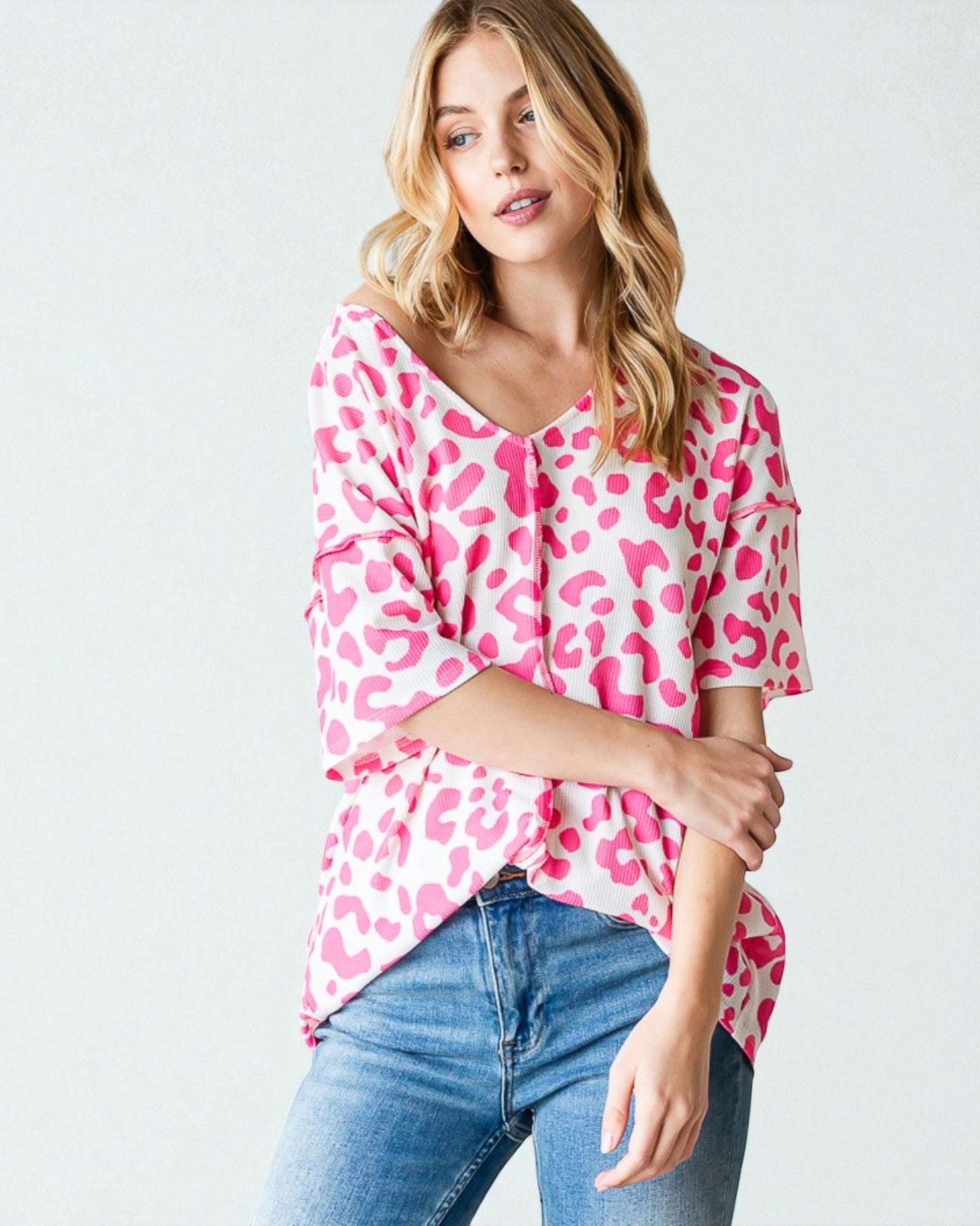 Woman wearing a pink leopard print top and blue jeans on a white background