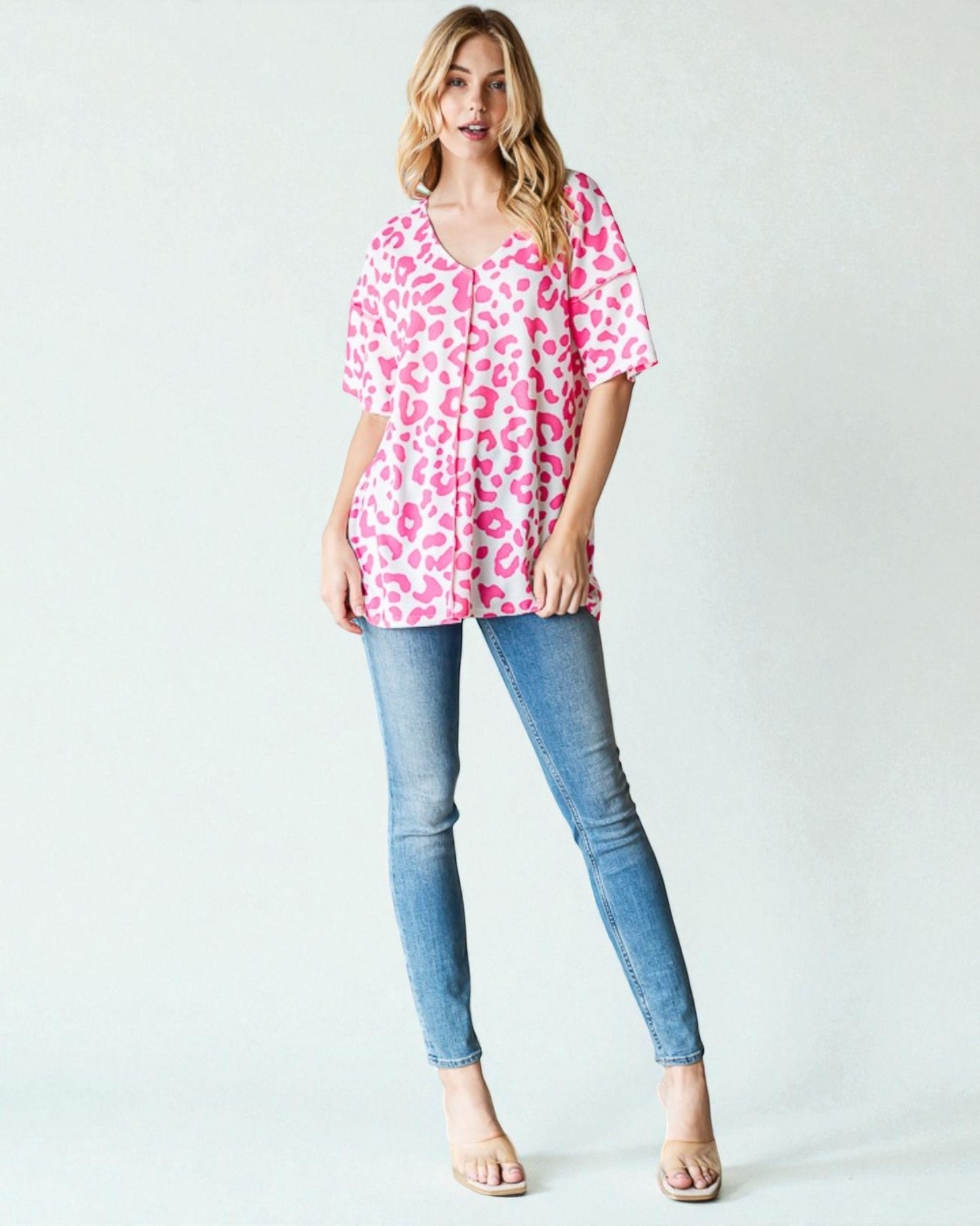Woman wearing a pink leopard print top and blue jeans on a white background