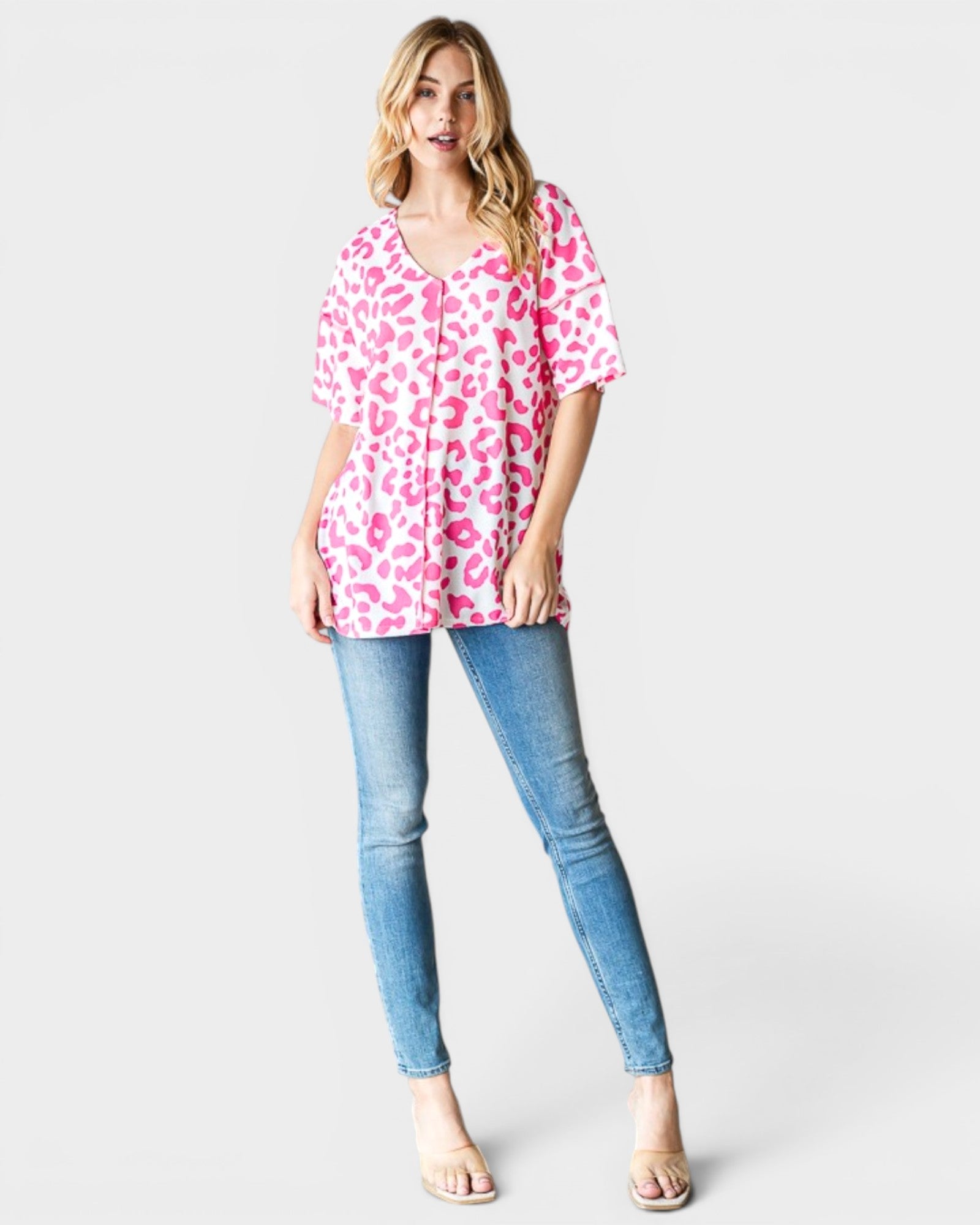 Woman wearing a pink leopard print top and blue jeans on a white background