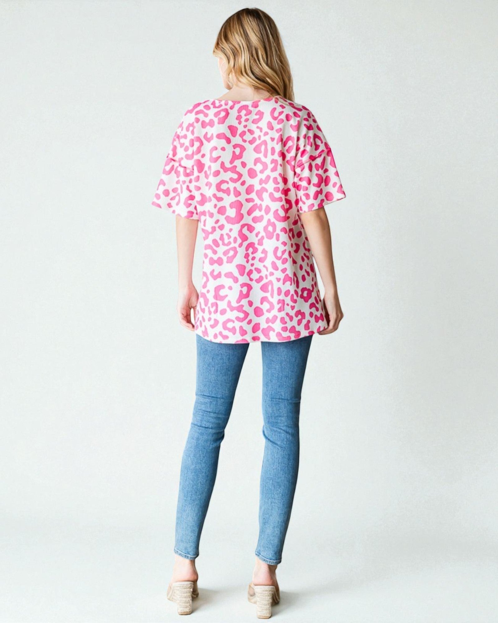 Person wearing a pink leopard print top and blue jeans on a white background