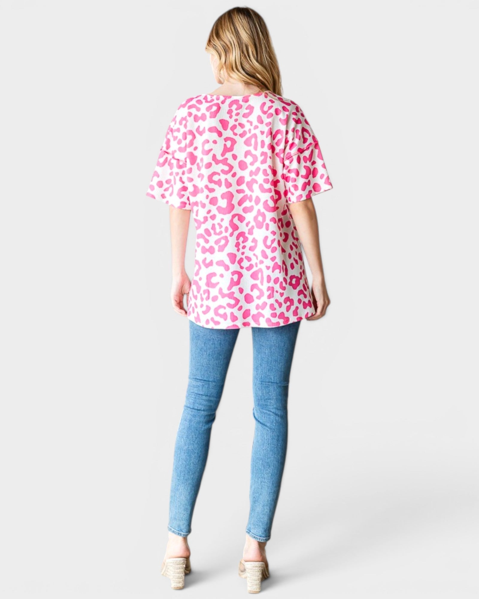 Woman wearing a pink leopard print top and blue jeans on a white background