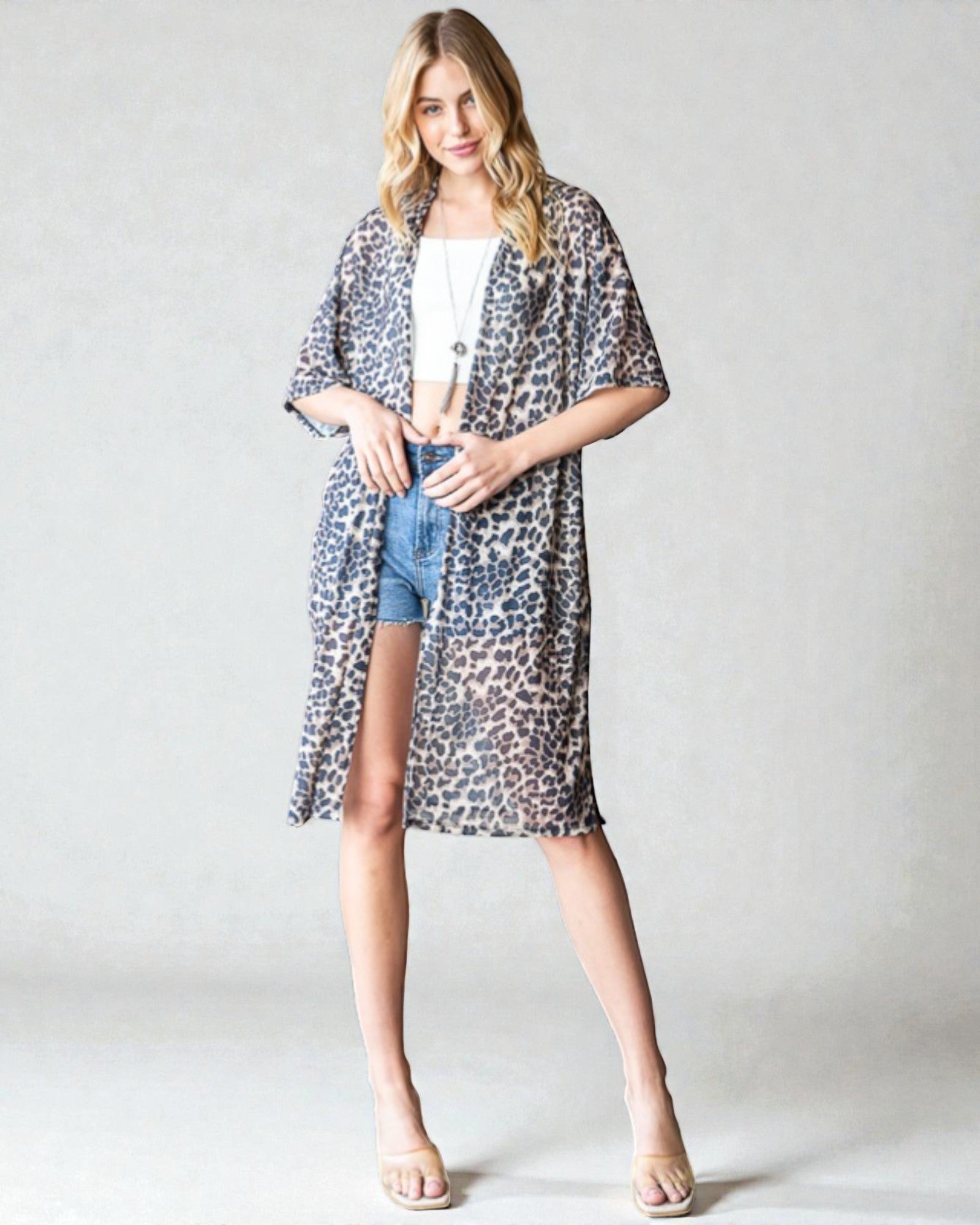 Woman wearing a leopard print kimono over a white top and denim shorts on a plain background