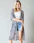 Woman wearing a leopard print kimono over a white top and denim shorts on a gray background