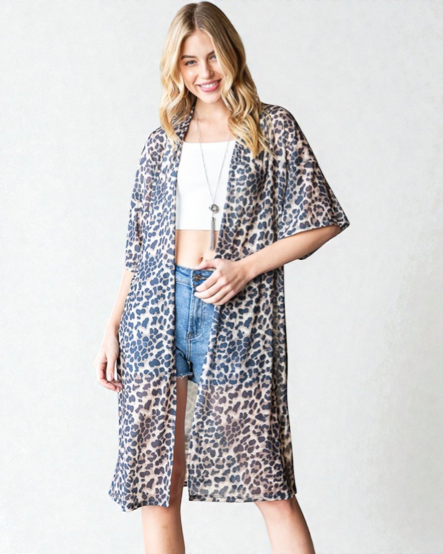 Woman wearing a leopard print kimono over a white top and denim shorts on a white background