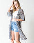 Woman wearing a leopard print kimono over a white top and denim shorts on a plain background