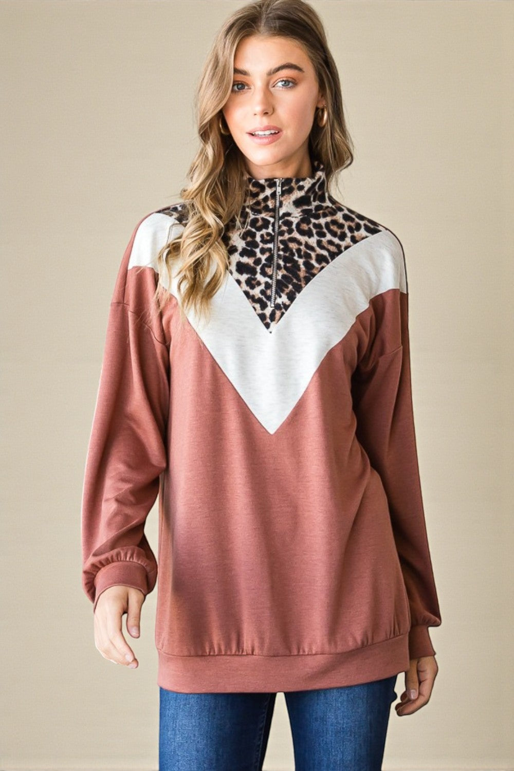 Woman wearing a brown and white top with a leopard print turtleneck underneath on a beige background