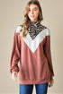 Woman wearing a brown and white top with a leopard print turtleneck underneath on a beige background