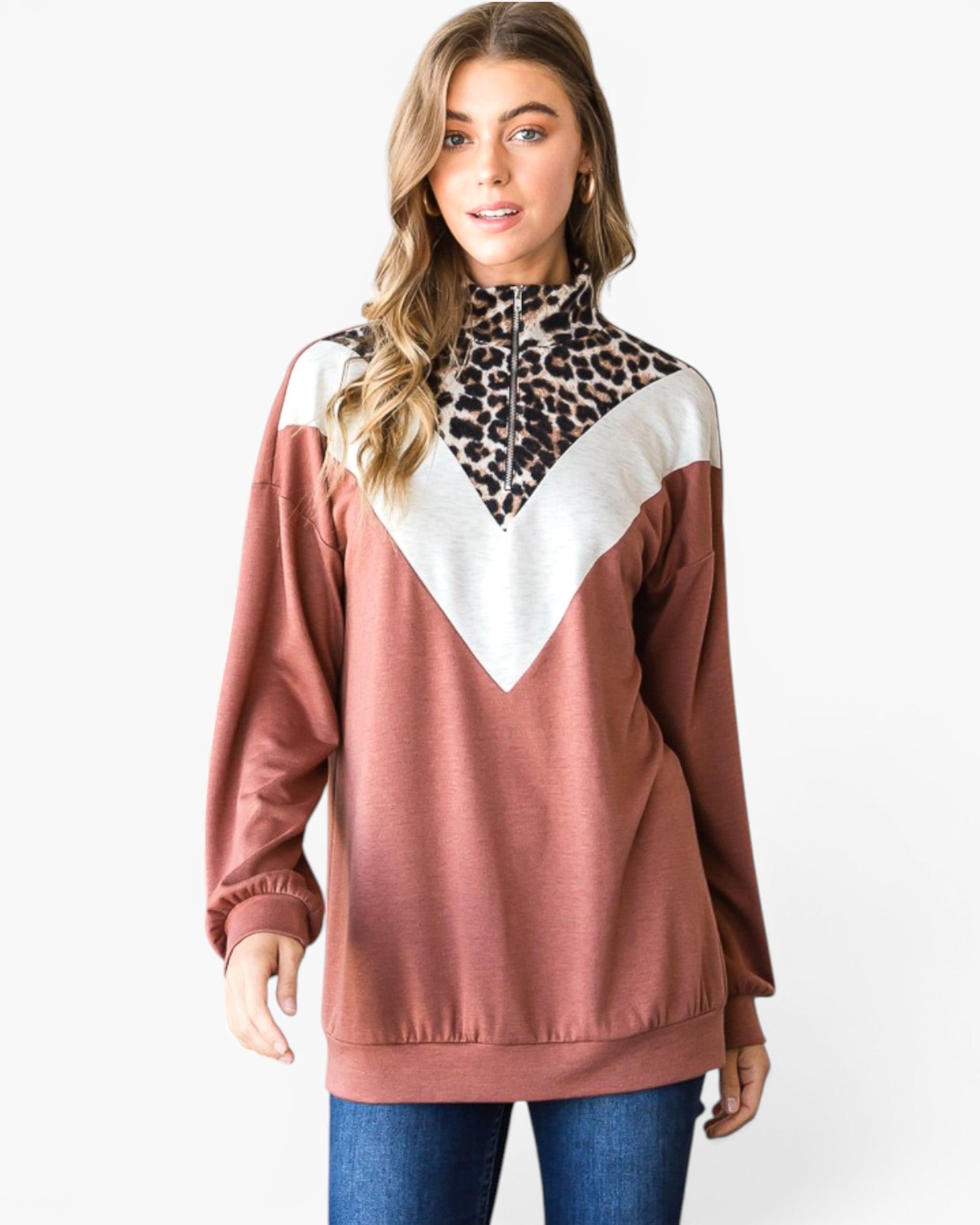 A woman modeling a long-sleeve colorblock sweatshirt with a leopard print yoke, white V-shaped chest panel, and dusty rose body, paired with blue jeans against a light gray background.