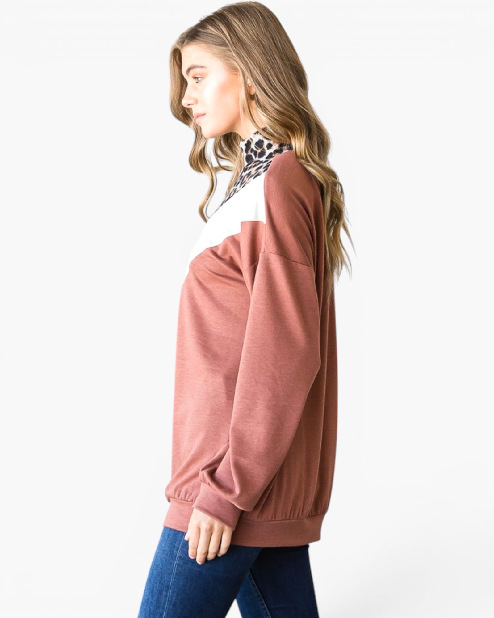 A woman shown in side profile wearing a dusty rose long-sleeve sweatshirt with a white yoke and a black-and-white patterned high-neck collar, paired with blue jeans against a plain white studio background.