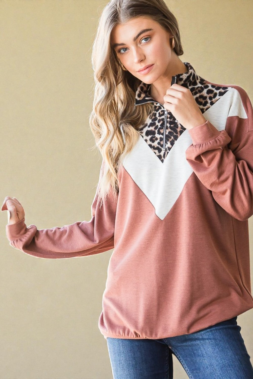 Woman wearing a pink long-sleeve top with a leopard print and white design, standing against a beige wall.
