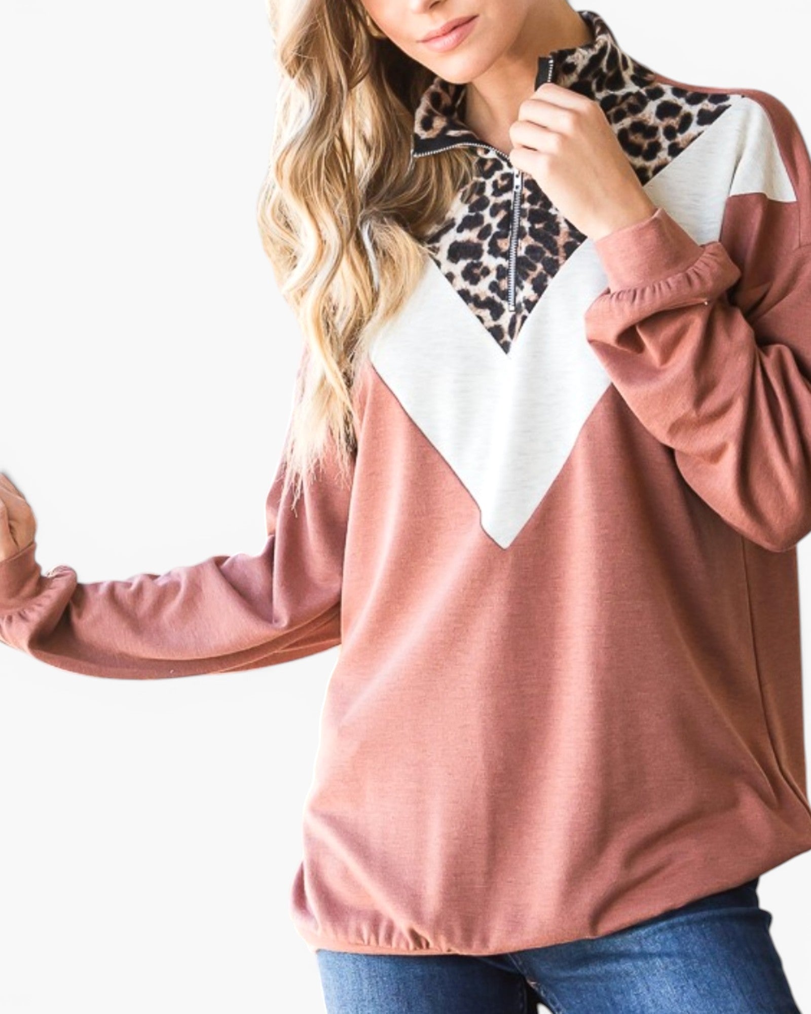 A woman wearing a color-blocked long-sleeve top with a dusty rose body, a white chevron section, and a leopard print collar, paired with blue jeans against a white background.