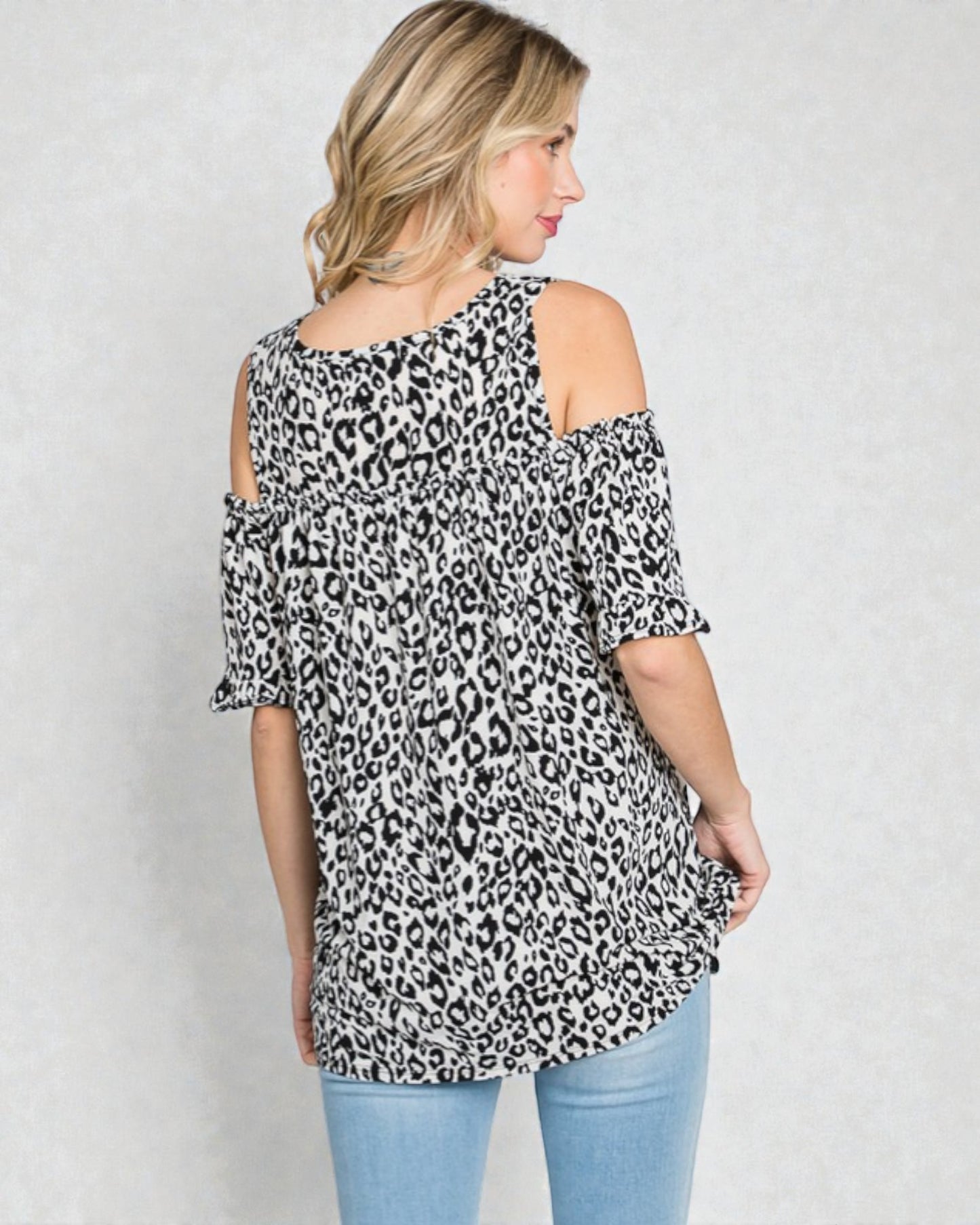 Woman wearing a leopard print off-shoulder top against a plain background