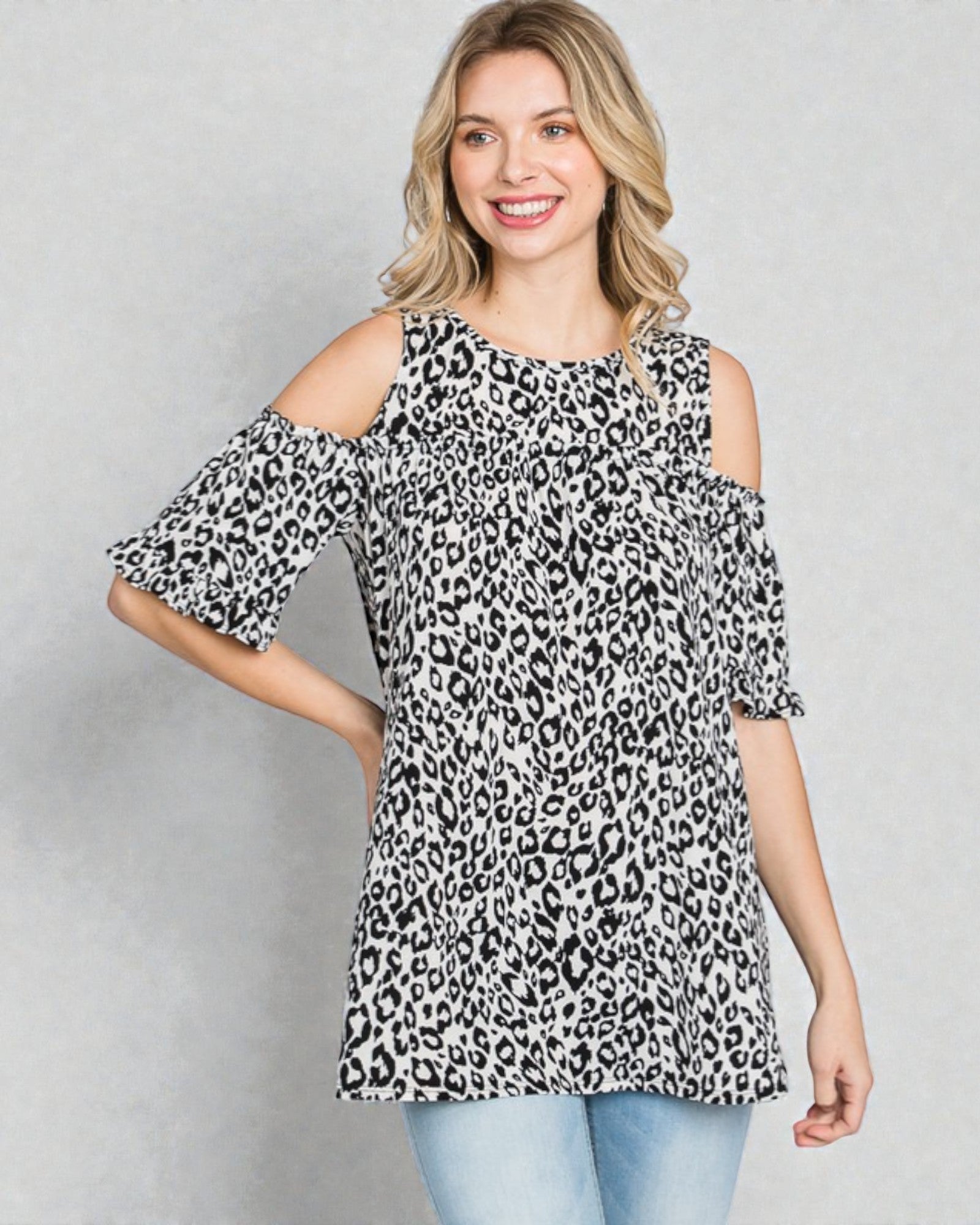 Woman wearing a leopard print cold shoulder top against a gray background