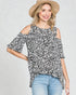 Woman wearing a leopard print cold-shoulder top and straw hat on a plain background