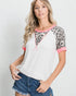 Woman wearing a white top with leopard print sleeves and pink trim, paired with denim shorts on a plain background.
