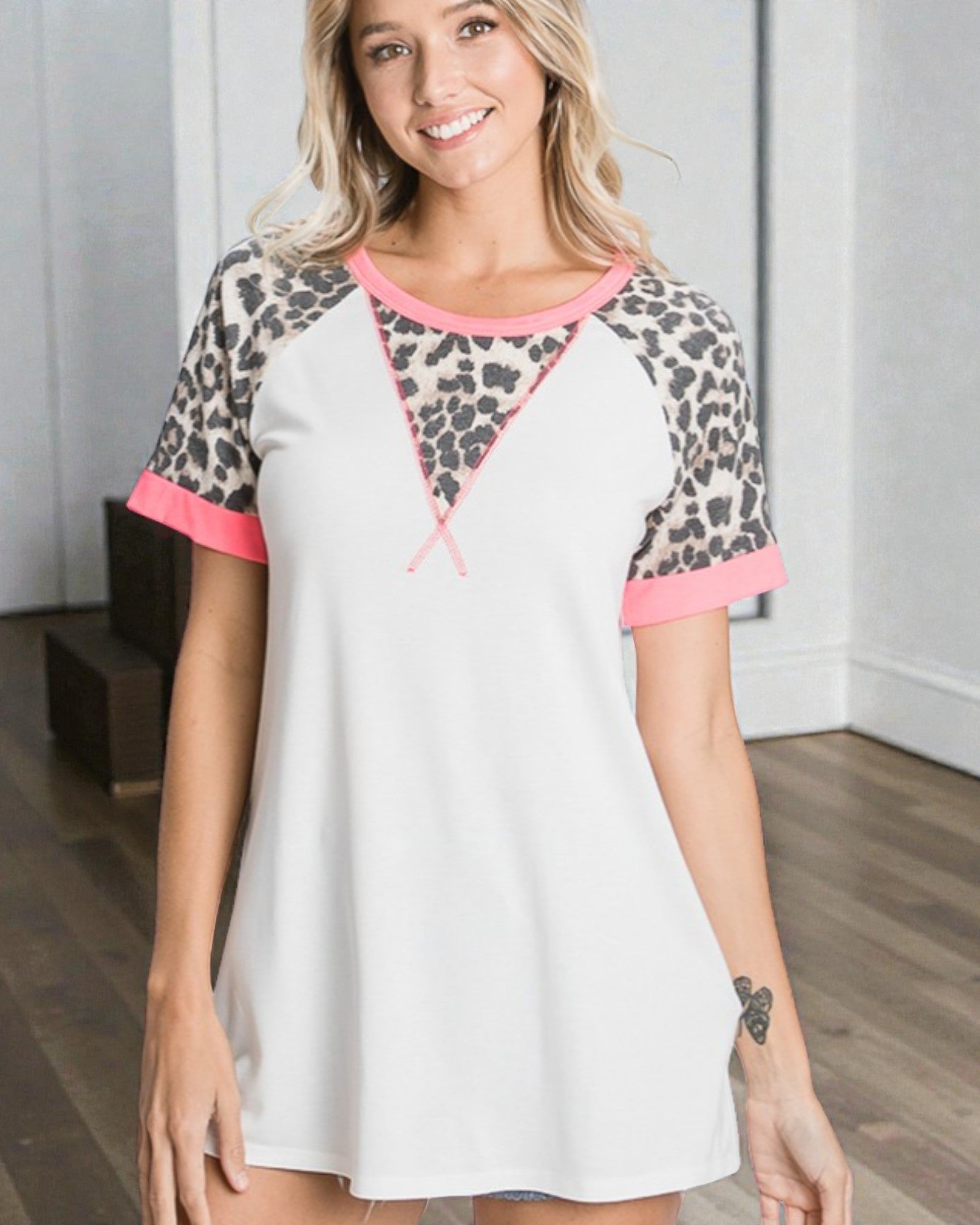 Woman wearing a white dress with leopard print sleeves and pink trim in a room.