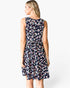 A woman modeling a sleeveless tiered dress from the back, featuring a navy blue base with a colorful pastel leopard print pattern, against a plain white studio background.