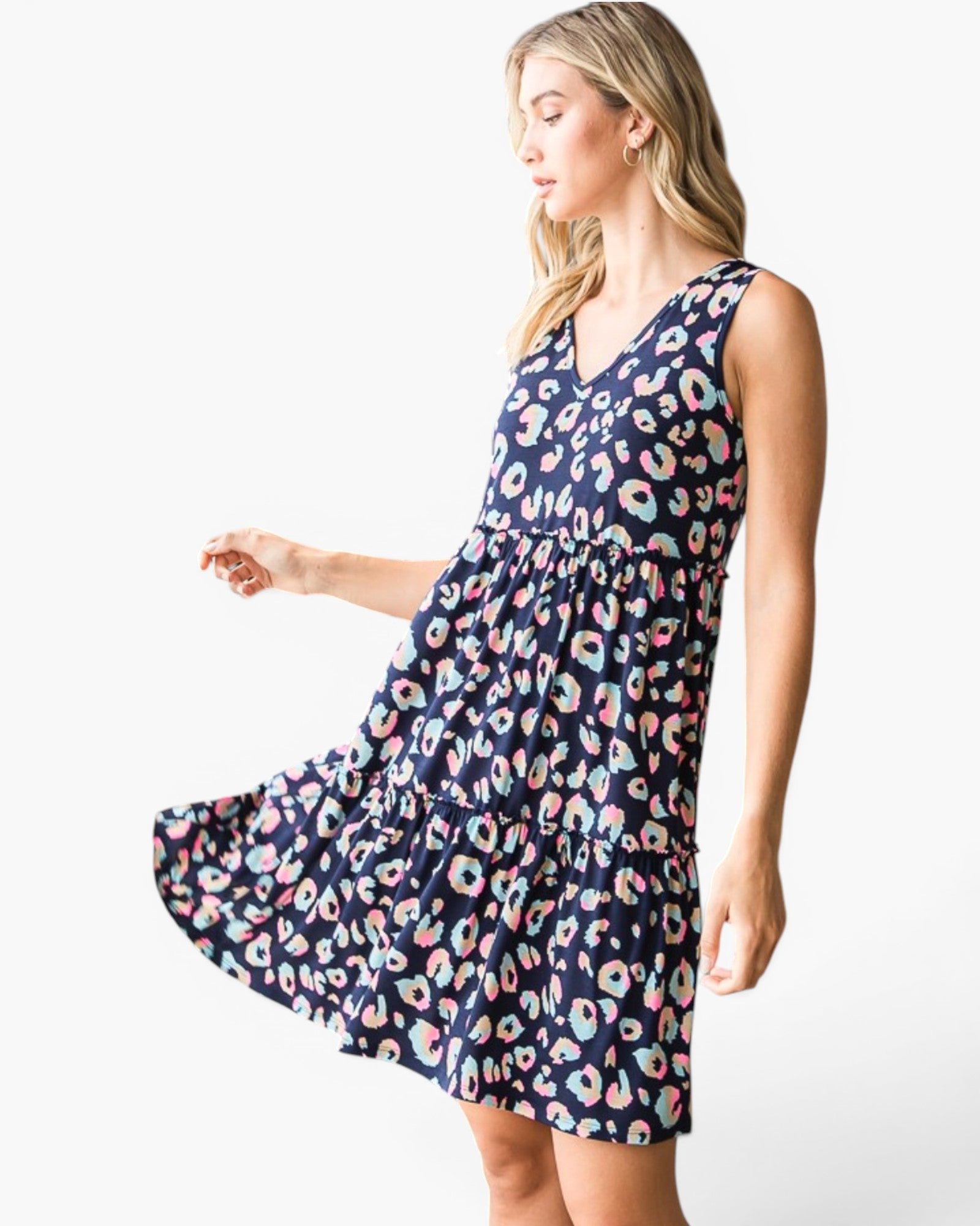 A woman modeling a sleeveless V-neck tiered dress with a navy blue background and a colorful donut print, set against a plain white studio background.