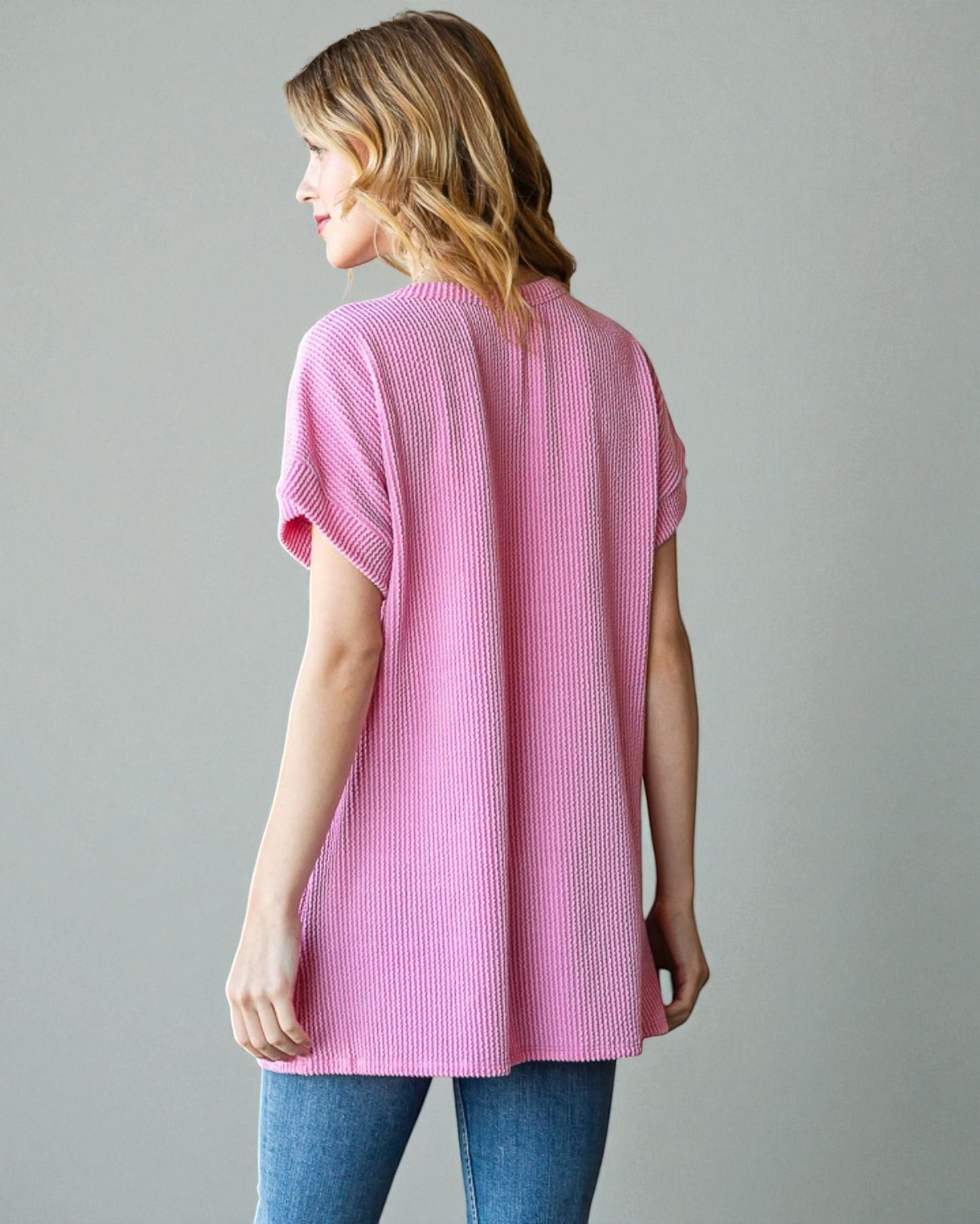 Woman wearing a pink ribbed sweater against a gray background