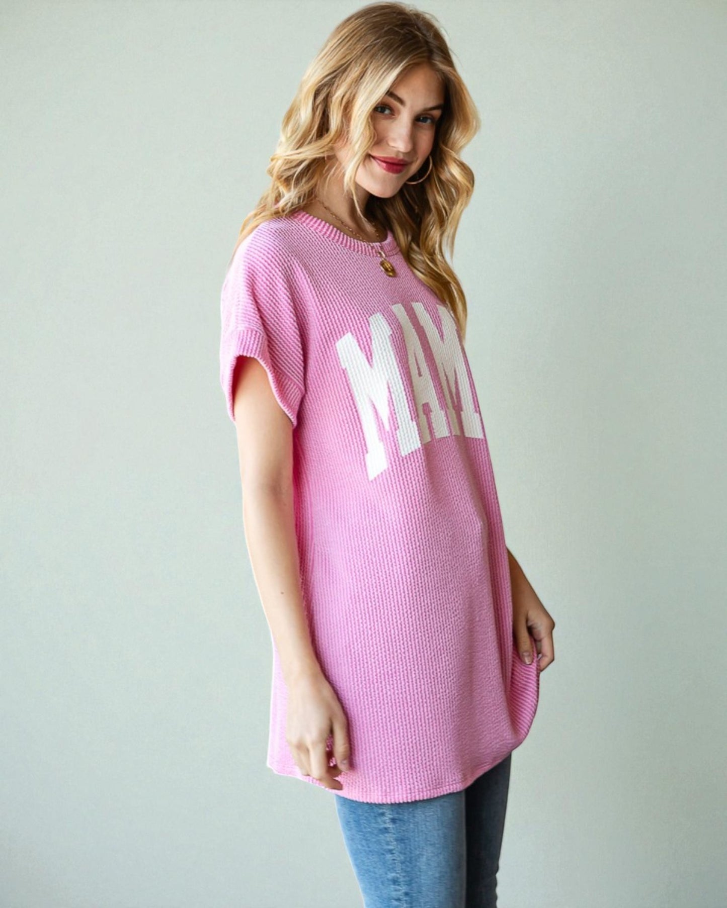 Woman wearing a pink oversized t-shirt with 'MAMA' text on a plain background