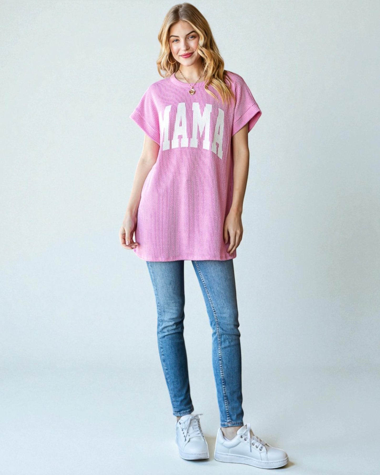 Woman wearing a pink oversized t-shirt with 'YAMA' text, blue jeans, and white sneakers on a light gray background