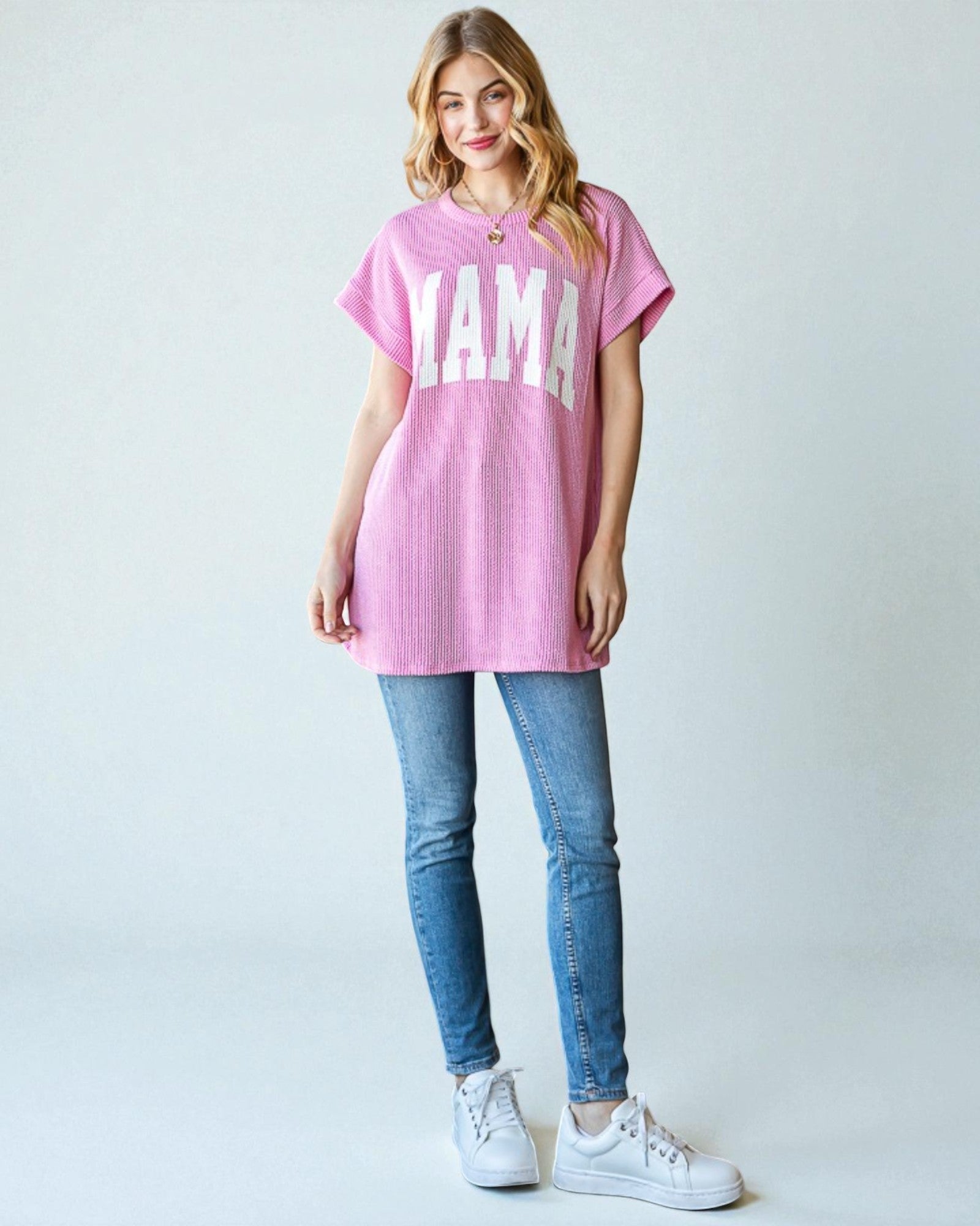 Woman wearing a pink oversized t-shirt with 'YAMA' text, blue jeans, and white sneakers on a light gray background