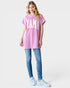 Woman wearing a pink oversized t-shirt with 'MAMA' text, blue jeans, and white sneakers on a light gray background.