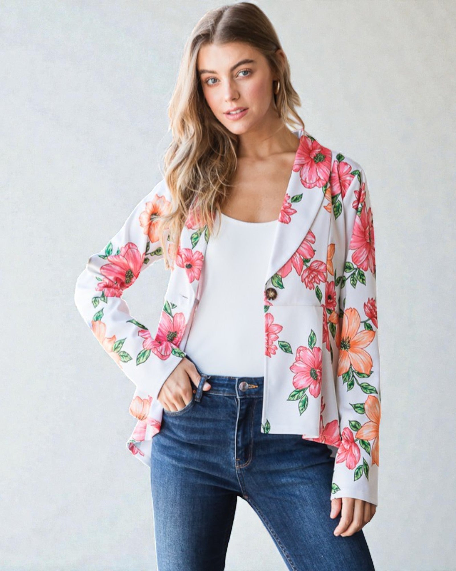 Woman wearing a floral kimono jacket over a white top and blue jeans on a plain background