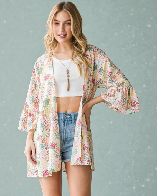 Woman wearing a floral kimono over a white top and denim shorts on a gray background