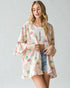 Woman wearing a floral kimono over a white top and denim shorts on a plain background