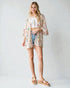 Woman wearing a floral kimono over a white top and denim shorts on a plain background