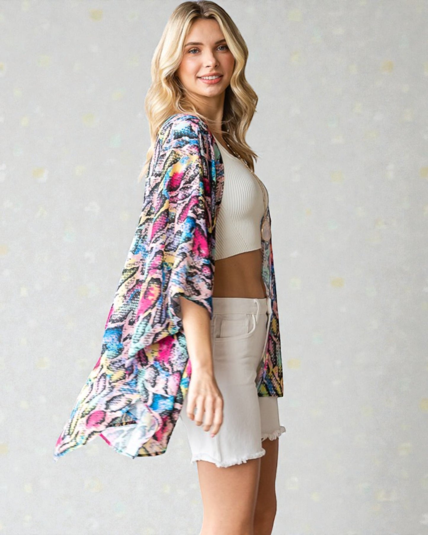 Woman wearing a colorful kimono-style garment over a white top and shorts on a light gray background.