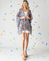 Woman wearing a colorful kimono-style garment against a light gray background with colorful confetti-like shapes.