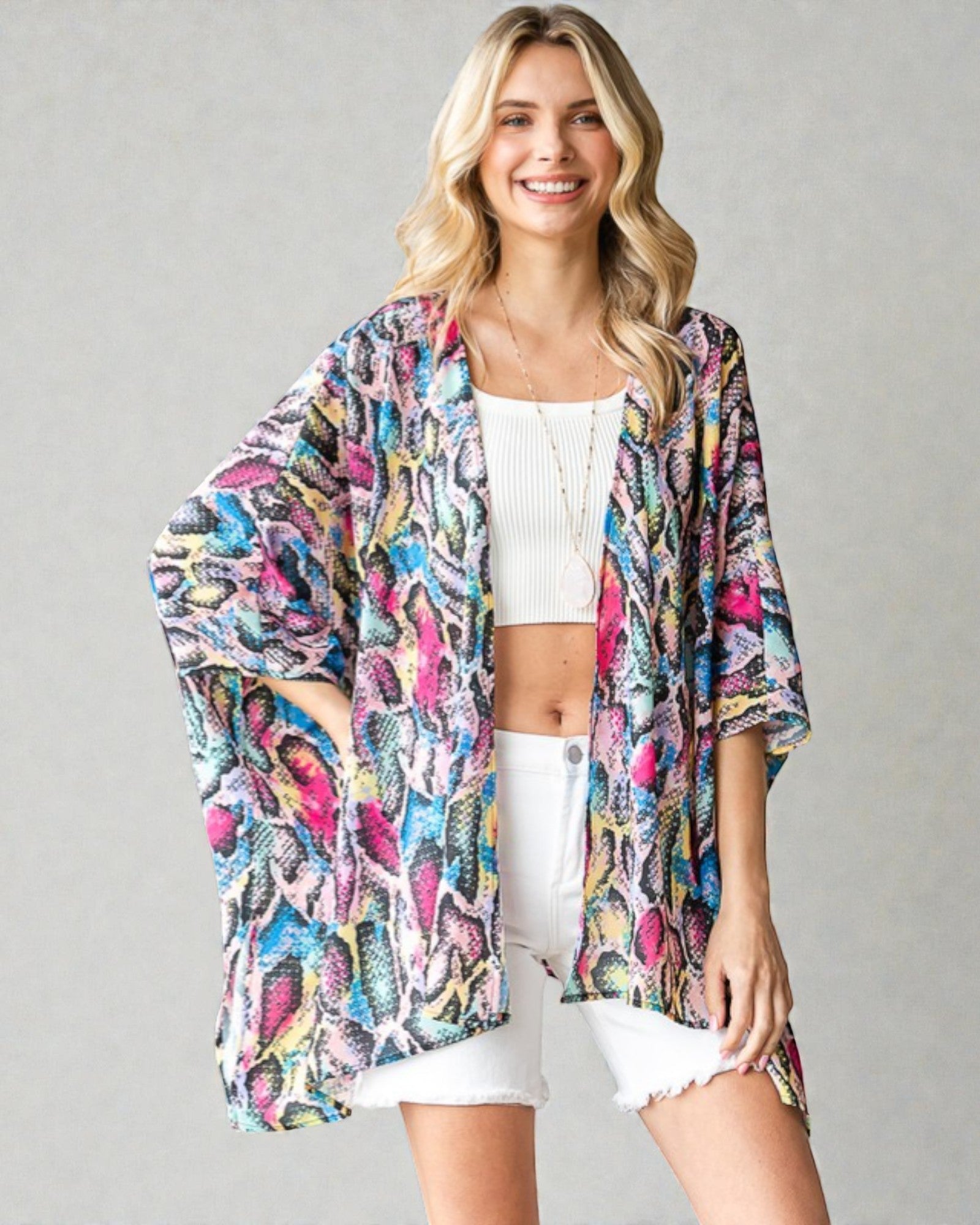 Woman wearing a colorful kimono-style jacket over a white outfit on a gray background