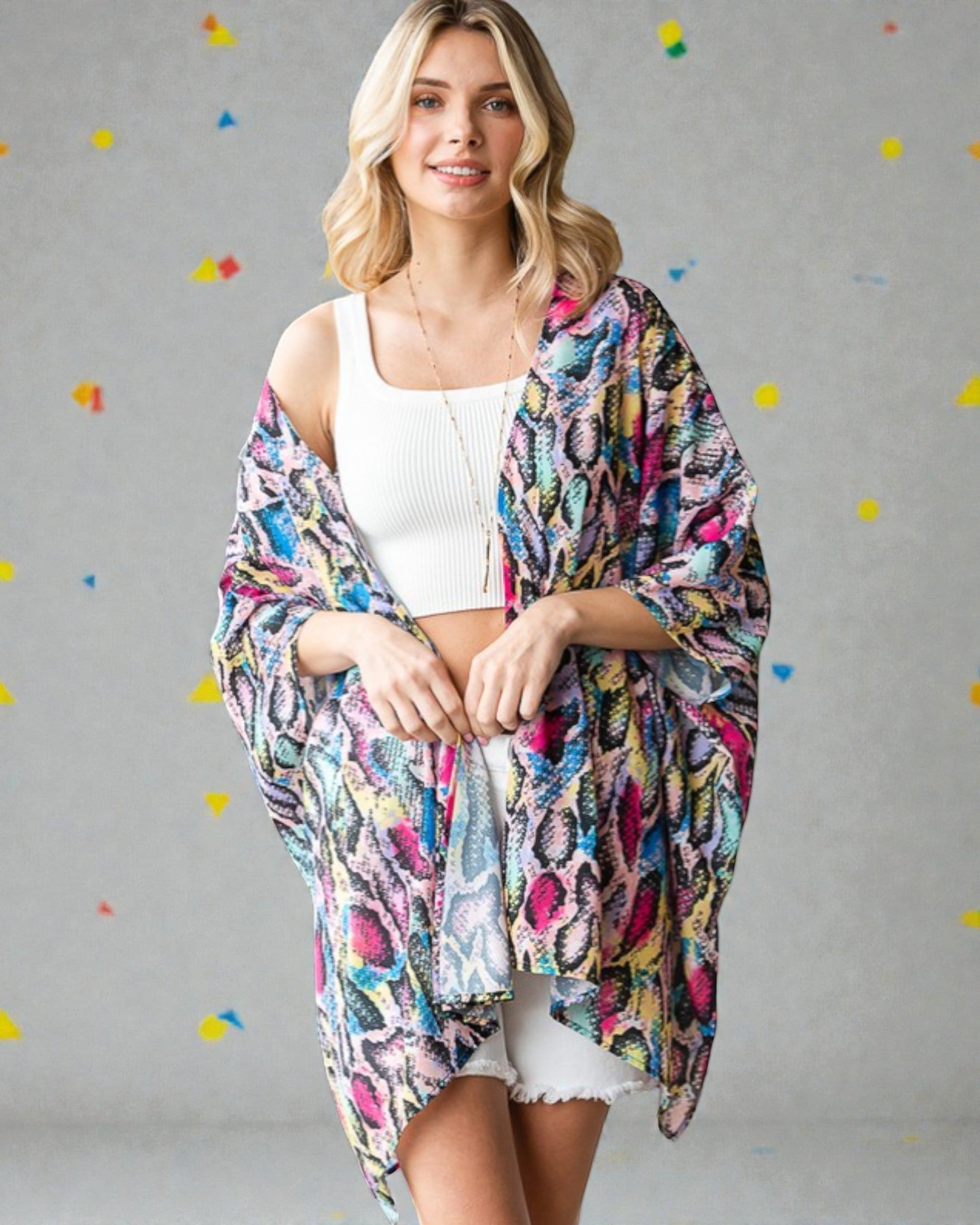 Woman wearing a colorful patterned kimono over a white top and skirt on a gray background with colorful dots.