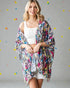 Woman wearing a colorful patterned kimono over a white top and skirt on a gray background with colorful dots.
