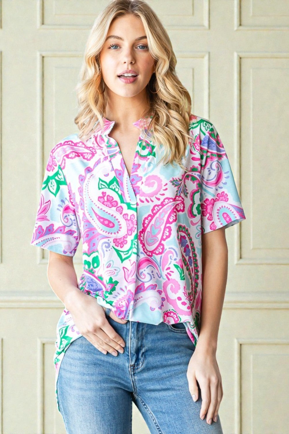 Woman wearing a colorful patterned shirt and jeans against a beige wall.