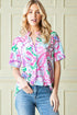 Woman wearing a colorful patterned shirt and jeans against a beige wall.