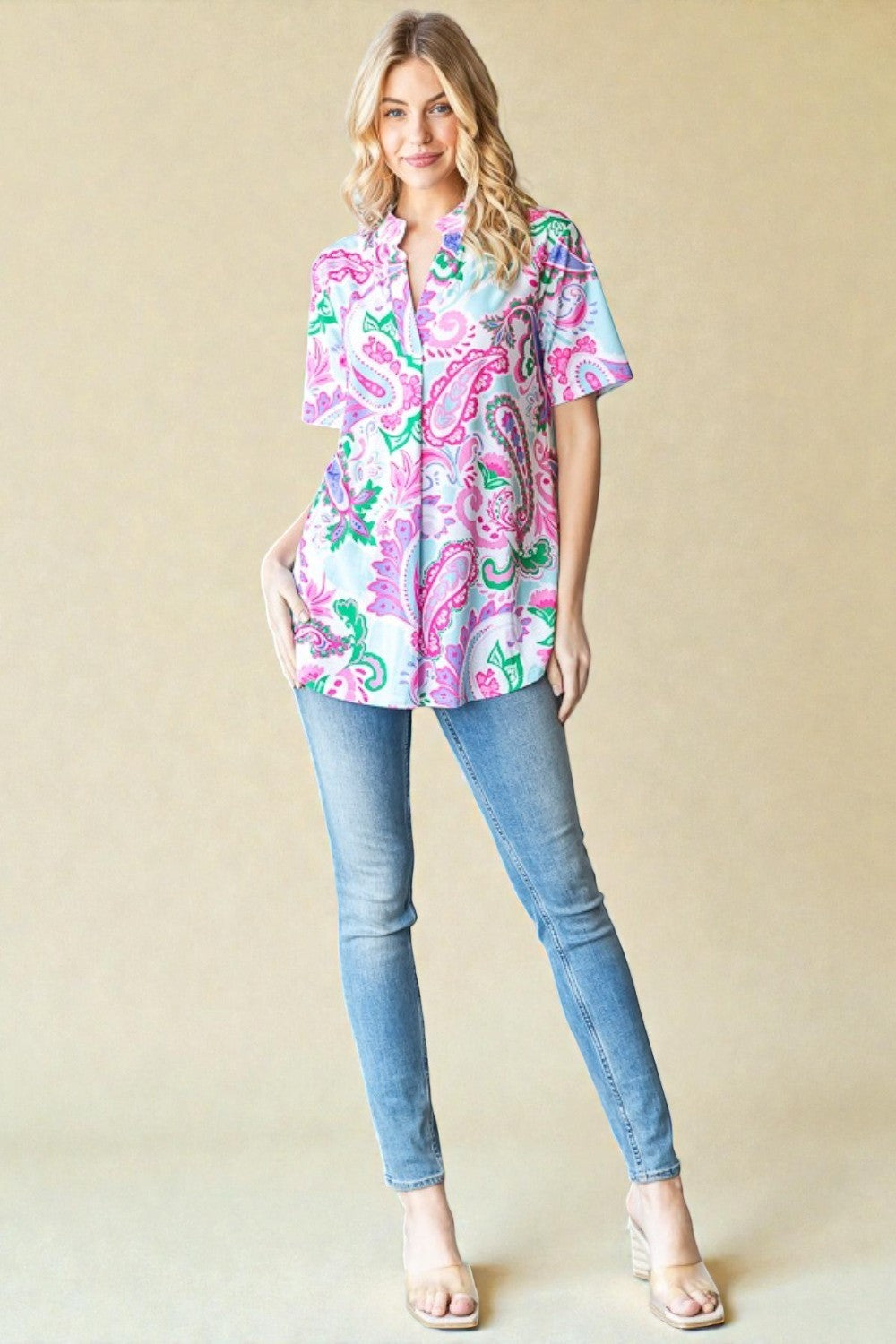 Woman wearing a colorful patterned blouse and blue jeans against a beige background