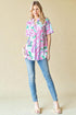 Woman wearing a colorful patterned blouse and blue jeans against a beige background