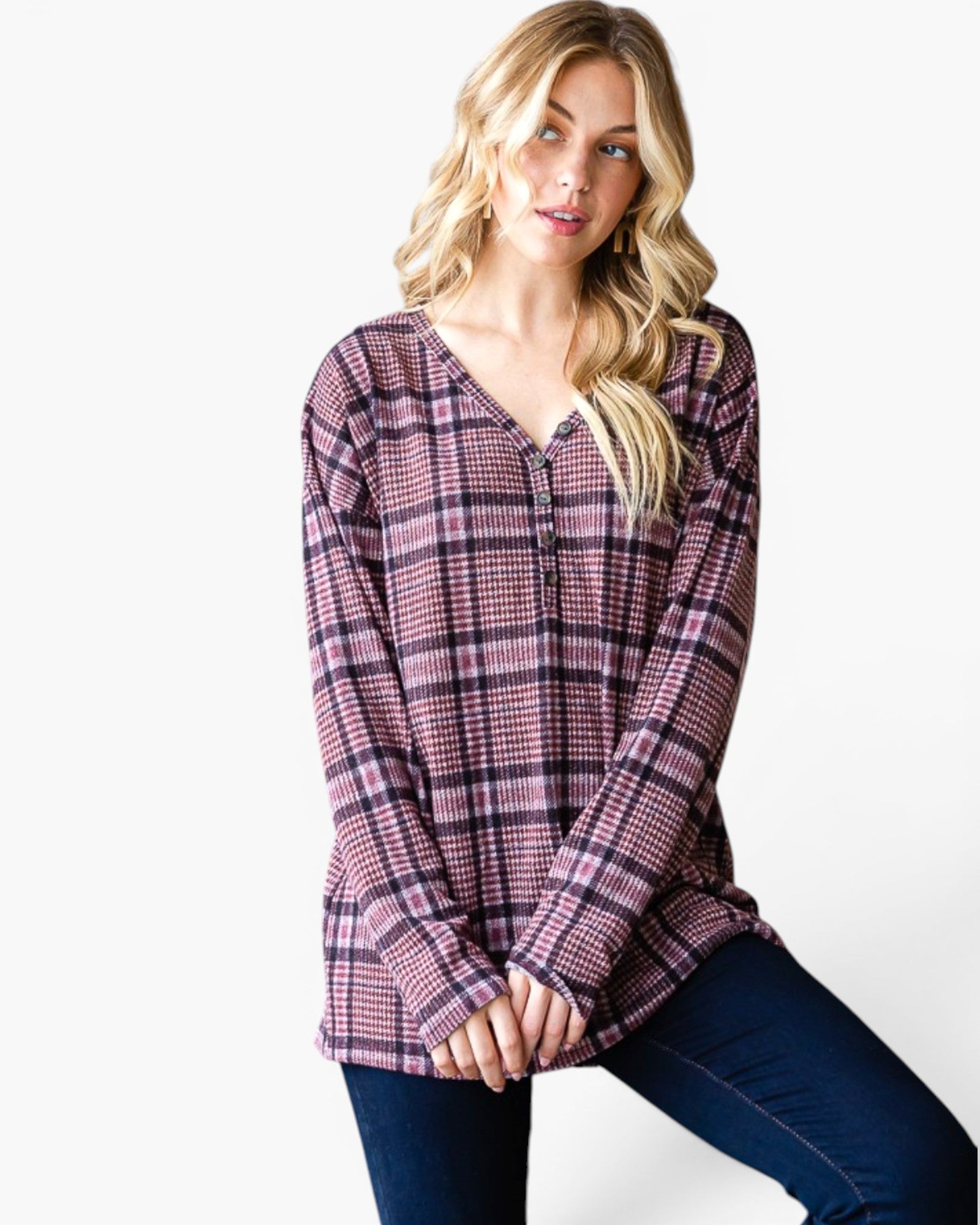 A woman wearing a long-sleeve plaid button-up top in a dusty purple and pink colorway, paired with dark blue jeans, posed against a clean white background.