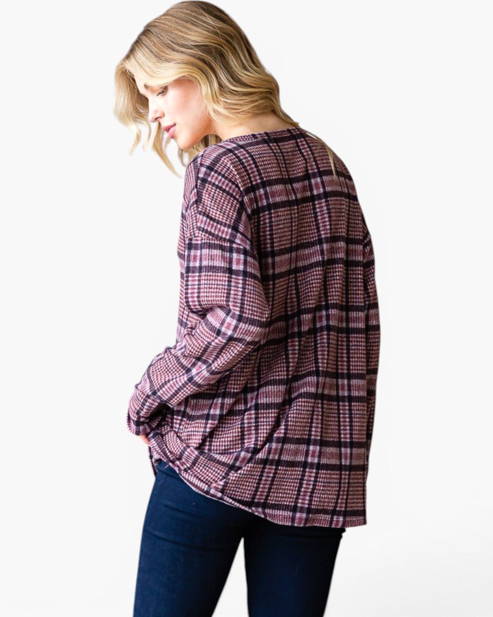 A woman wearing a pink and purple plaid long-sleeve top with dark blue jeans, photographed against a plain white background.