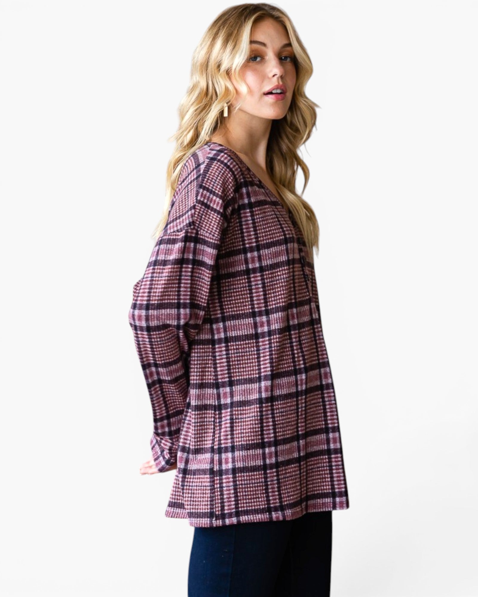 A woman modeling a long-sleeve plaid top in pink, purple, and black, paired with dark blue jeans, against a plain white studio background.