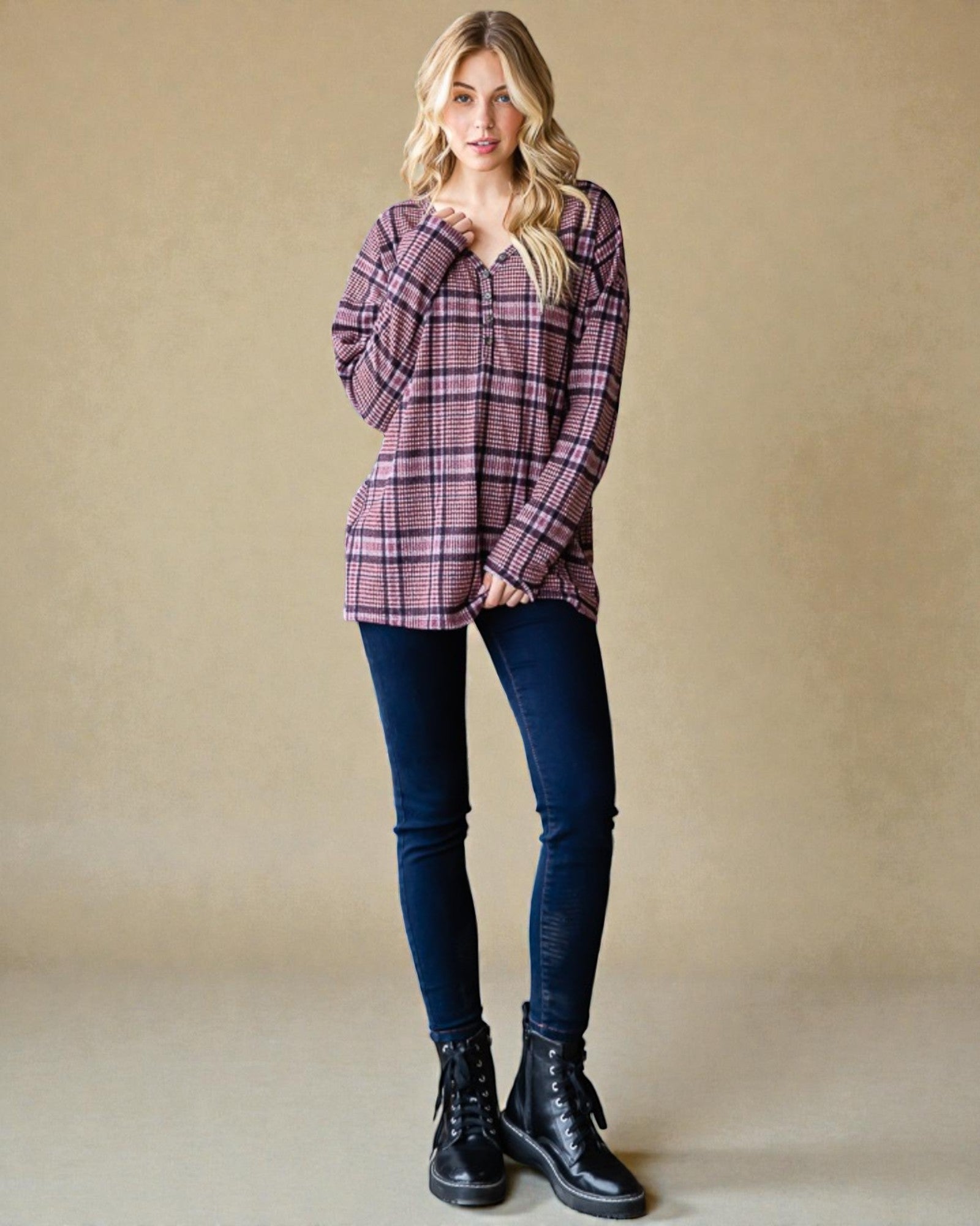 Woman wearing a plaid shirt, dark jeans, and black boots against a beige background