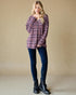 Woman wearing a plaid shirt, dark jeans, and black boots against a beige background