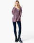 A woman modeling a long-sleeve plaid button-up shirt in purple and pink tones, paired with dark blue skinny jeans and black lace-up ankle boots, against a plain white studio background.