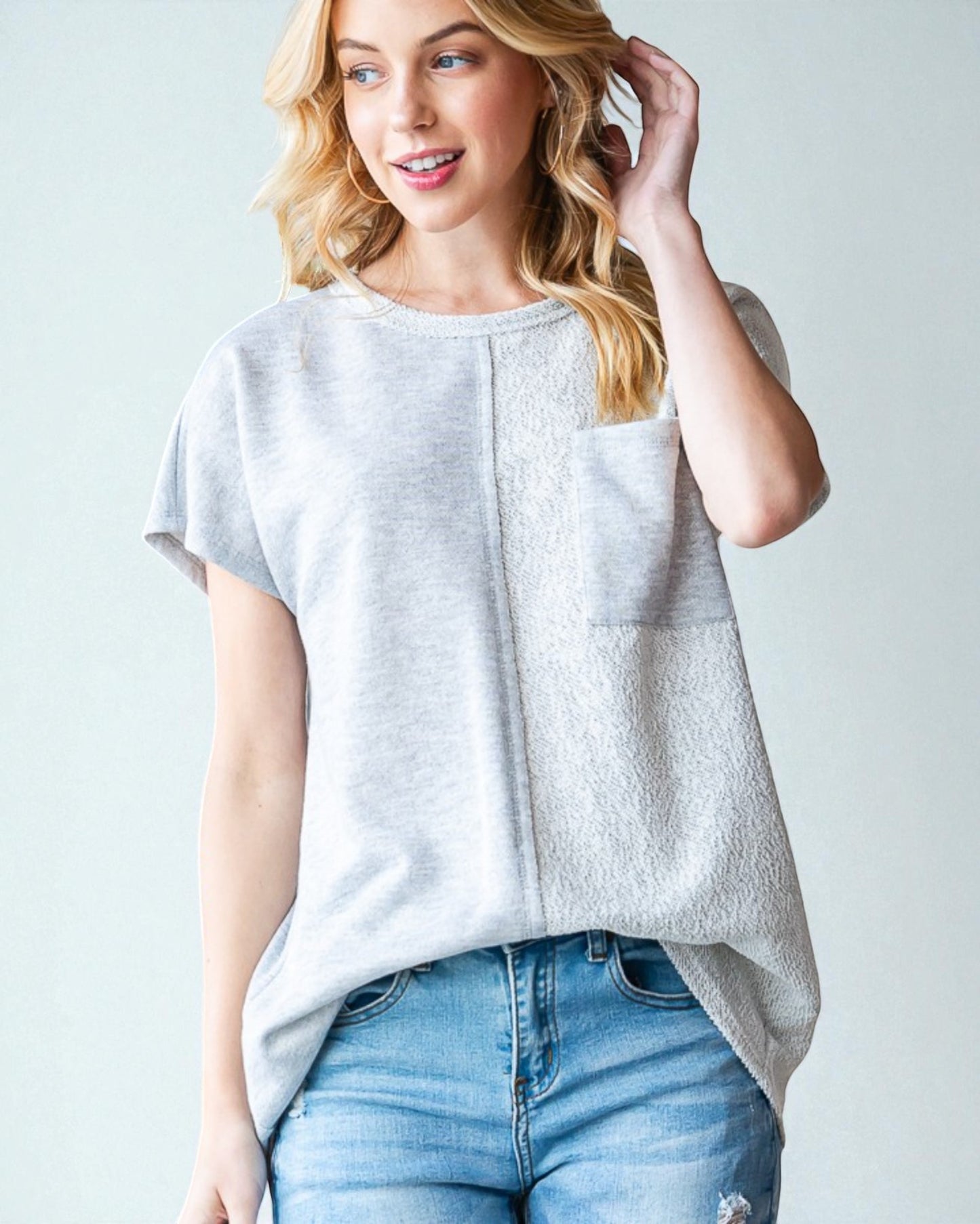 Woman wearing a light gray t-shirt with a pocket and blue jeans on a plain background