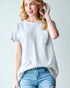 Woman wearing a light gray t-shirt with a pocket and blue jeans on a plain background