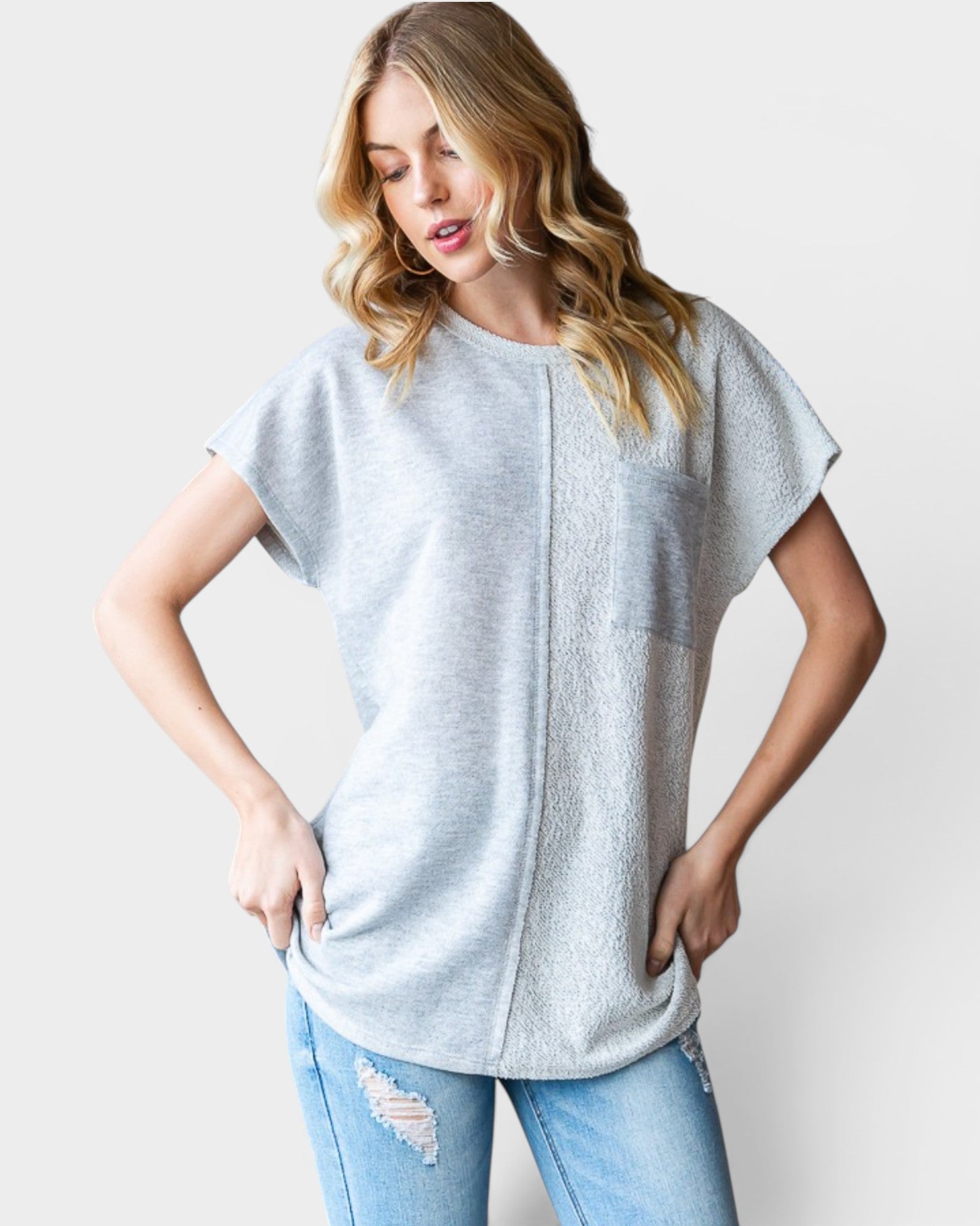 Woman wearing a light gray oversized t-shirt and blue jeans on a plain background