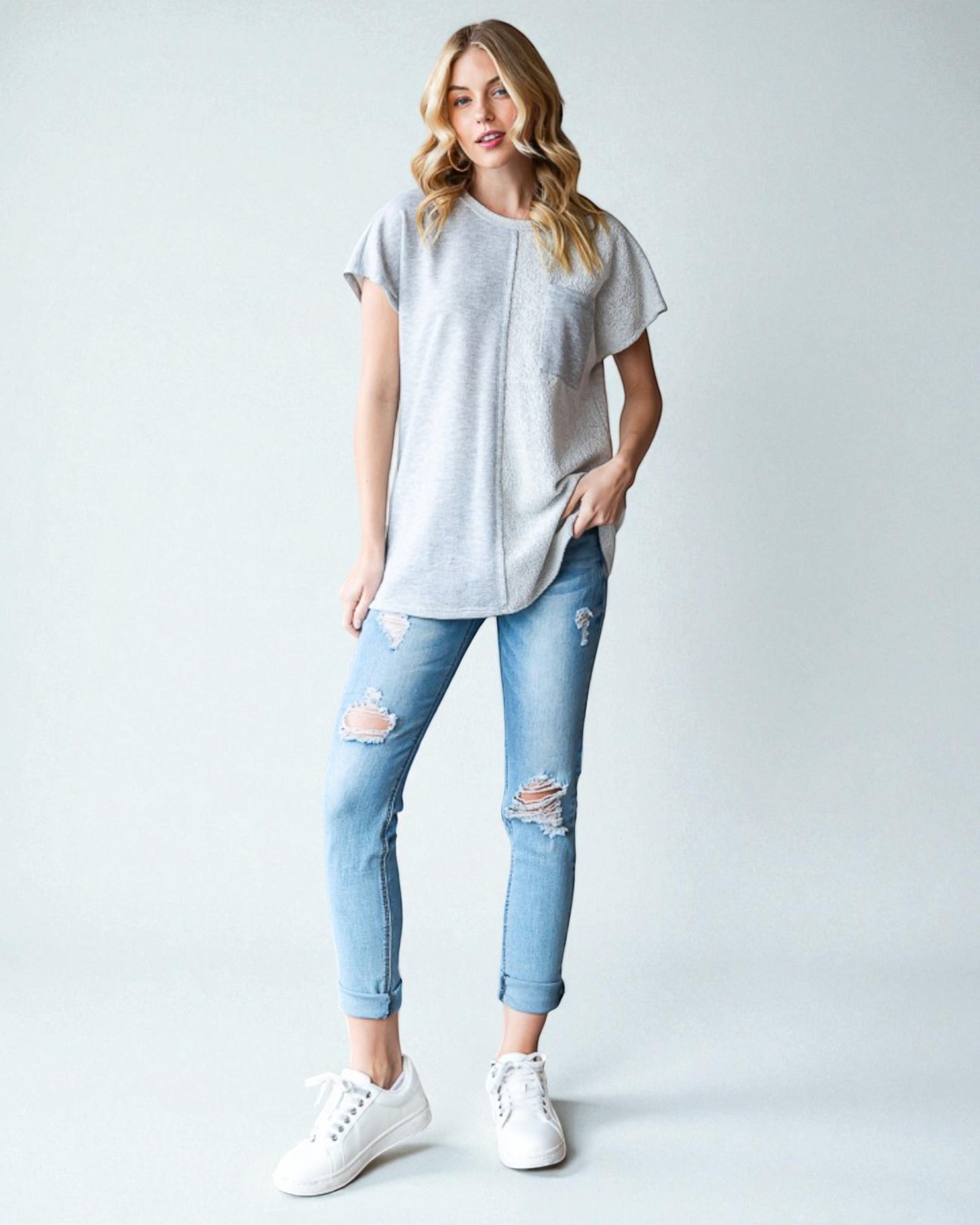 Woman wearing a light gray t-shirt and distressed blue jeans on a white background